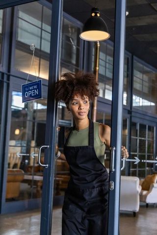 Barista opening glass doors and welcoming customers at industrial coffeehouse entrance