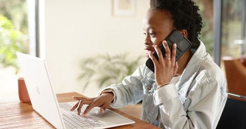African american woman working from home using laptop and phone, remote work productivity