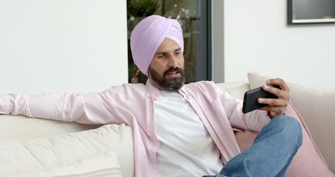 Indian man in pink shirt relaxing with smartphone at home