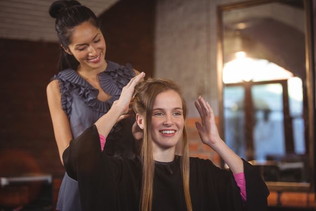 Female hairdresser styling a customer's hair at a salon. The customer is smiling and appears happy with the service. This image can be used for promoting beauty salons, hairstyling services, hair care products, and professional grooming. It highlights the interaction between the stylist and the client, showcasing the professional and friendly environment of the salon.