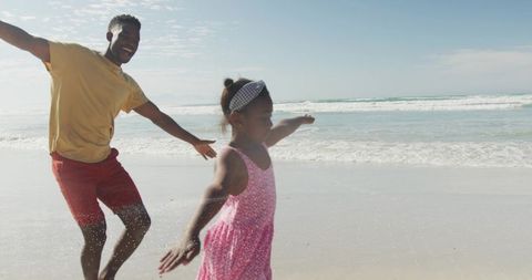 Father and daughter running on sunny beach splashing in surf laughing together