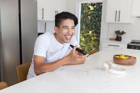 Laughing african american man holding smartphone at modern bright white kitchen island