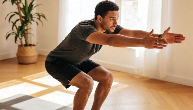 Man performing deep bodyweight squat at home during morning workout with wrist tracker