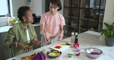 Diverse friends preparing healthy plant-based meal on marble island chopping avocado