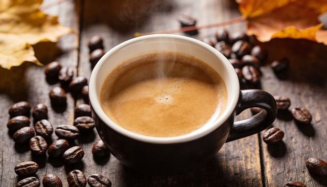Steaming Espresso Cup with Creamy Crema on Rustic Wooden Table with Coffee Beans