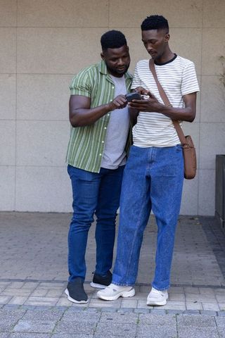 Two african men checking smartphone together, leaning in and pointing while sharing directions