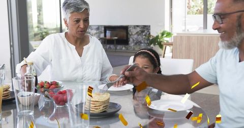 Multigenerational family sharing pancakes with gold confetti in modern bright kitchen