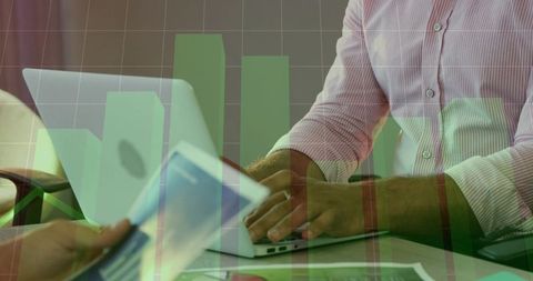 Hands Typing on Laptop with Tablet and Green Finance Bar Charts Showing Growth