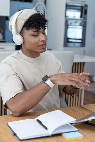 African american man wearing beanie and headphones working remotely at kitchen table