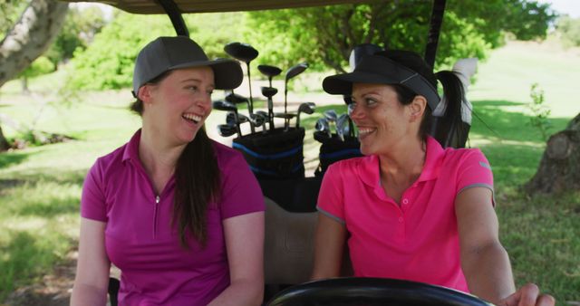 Two caucasian women playing golf riding a golf cart talking and laughing. golf cart and clubs in background. golf sports hobby healthy lifestyle.