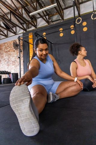 Diverse women stretching together on gym floor reaching forward in activewear and trainers