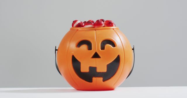 Perfect for Halloween-themed promotions, this vibrant image shows a pumpkin bucket filled with spooky candy eyeballs. Ideal for advertisements, social media posts, and holiday blog articles. The combination of orange pumpkin and eerie candy makes it suitable for capturing the festive and spooky atmosphere of Halloween.