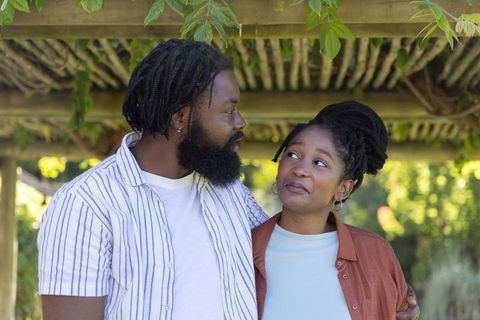 African american couple sharing warm eye contact under pergola in sunlit garden, casual