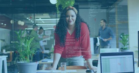 Female tech lead leaning over desk with code overlay in modern collaborative office