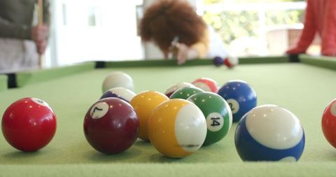 Friends playing pool in bright game room, woman aiming cue at rack of billiard balls
