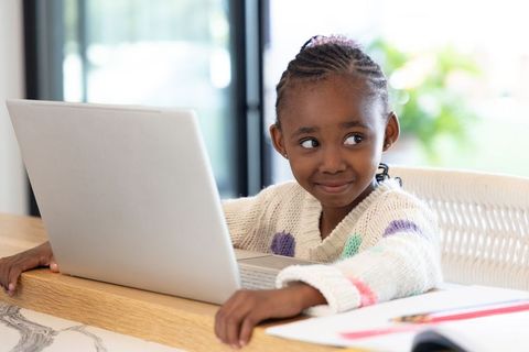 African American girl studying on laptop at home, smiling and learning in cozy sunlit room