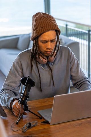 African american podcaster recording remote show with laptop, microphone and headphones