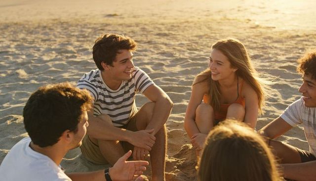 Teens chatting and laughing on beach at sunset sitting in circle relaxed golden hour