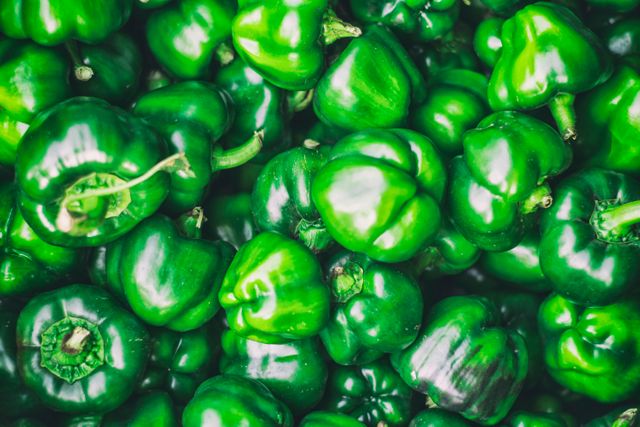 Fresh green bell peppers filling frame, showcasing vibrant and glossy appearance. Ideal for promoting healthy eating, fresh produce, vegetarian or vegan lifestyles, and farm markets. Can be used in grocery store marketing, food blogs, and recipe websites.