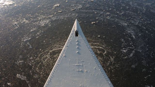 Bow cutting through thin ice floes over dark winter water, riveted metal prow detail