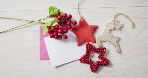 Flat-lay holiday cards featuring rustic ornaments and red berry sprig on light wood