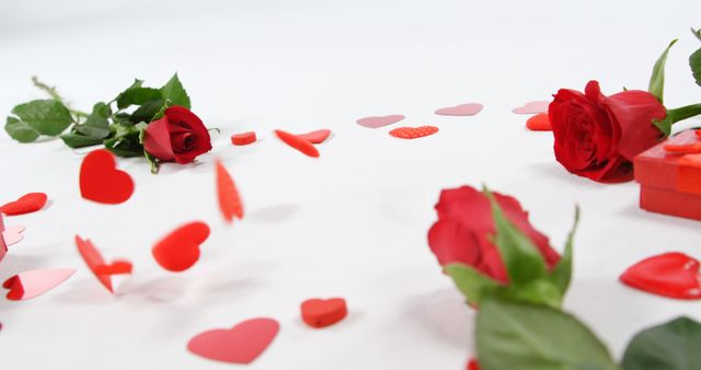 Red roses and heart-shaped confetti scattered against a white background, representing love and Valentine's Day. Ideal for Valentine's Day promotions, romantic event invitations, greeting cards, or ads related to love and romance.