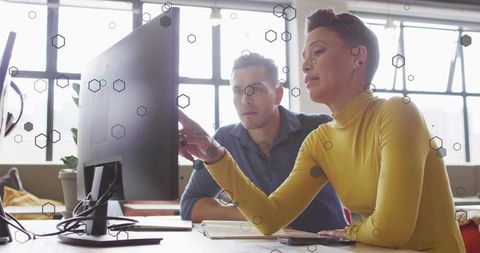 Mature professional pointing and guiding coworker at desktop monitor in modern open-plan office