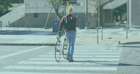 Man pushing bicycle across sunlit city crosswalk wearing red plaid jacket and backpack