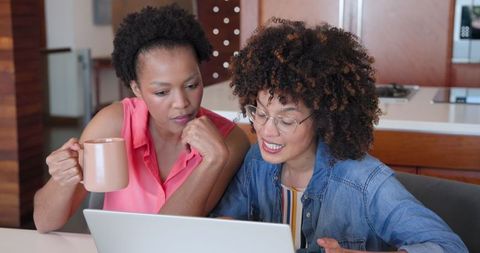 Diverse Female Couple Laughing and Enjoying Coffee While Reading Laptop Together