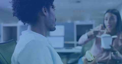 Casual office lunch conversation between coworkers sharing food in open-plan workspace