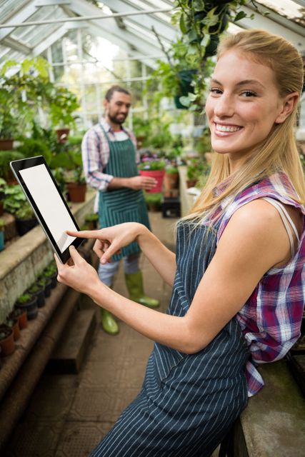 Portrait of happy young female gardener using digital tablet at greenhouse
