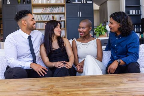 African american woman and friends sitting on couch in formal wear sharing conversation