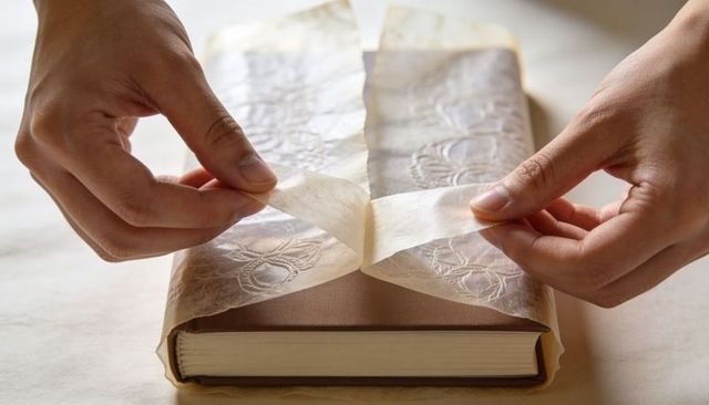 Careful hands wrapping vintage hardcover book with translucent embossed tissue