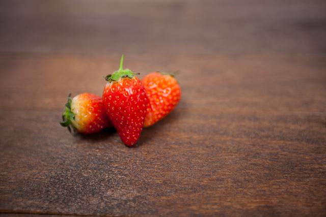 This image features a close-up view of fresh strawberries placed on a wooden table. The vibrant red color of the strawberries contrasts with the rustic wooden surface, making it visually appealing. This image can be used for promoting healthy eating, organic food products, recipes, or as a decorative element in food blogs and websites.