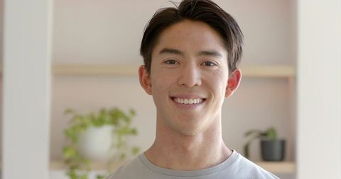 Young asian man smiling in minimalist room with potted plant decor