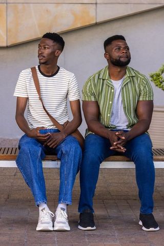 Two african men sitting on bench in urban plaza wearing striped shirts and jeans