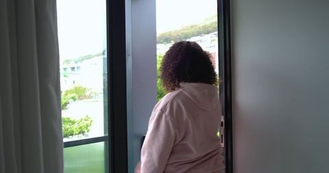 African american woman standing on balcony wearing pink hoodie overlooking hillside