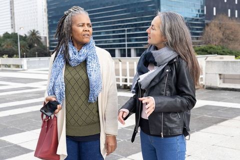 Mature women walking and talking on urban plaza wearing scarves and carrying red tote