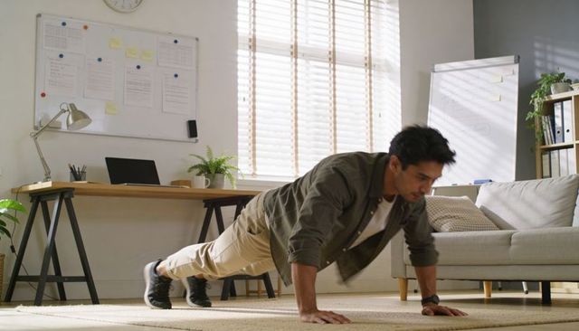 Man doing pushups in home office during remote workday, fitness break at desk with laptop