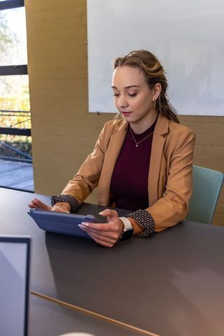 Young professional using tablet in modern office wearing tan blazer and smartwatch