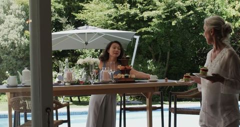 Women preparing elegant poolside gathering with desserts and drinks