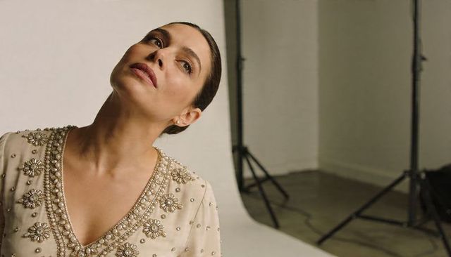 Elegant woman tilting head wearing beaded cream blouse with pearl embellishments