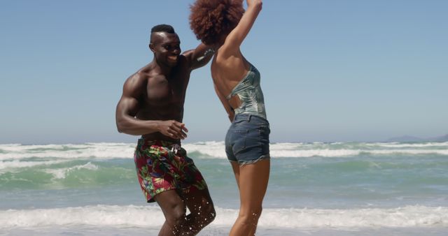 African American couple dancing and enjoying themselves by the ocean during a summer vacation. Useful for travel and tourism promotions, lifestyle blogs, summer vacation marketing, and leisure activity advertisements.