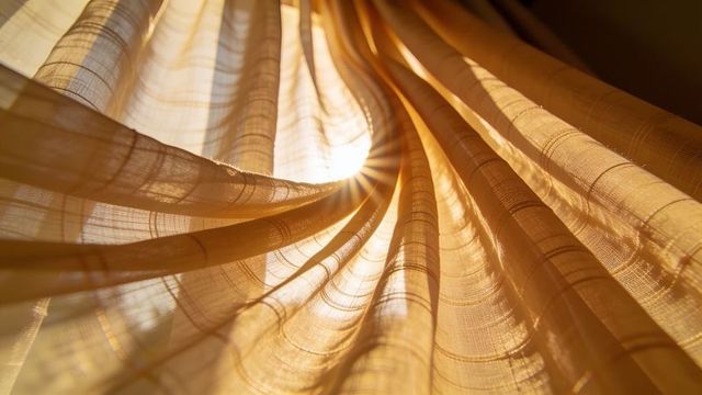 Golden sheer curtains filtering sunlight, backlit flowing draped fabric texture and glow
