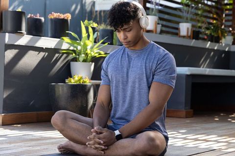 African american man meditating and listening with headphones on sunlit patio deck