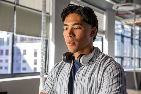 Young asian professional wearing headphones standing in modern urban office interior