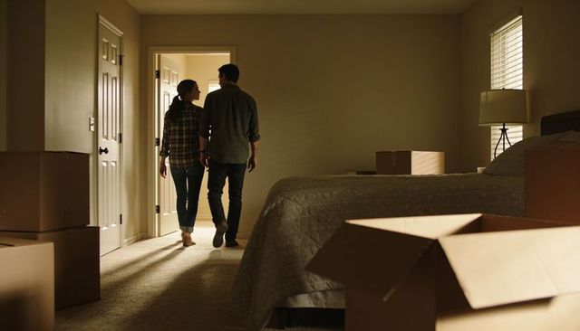 Young couple walking into bedroom amid moving boxes and warm late afternoon light