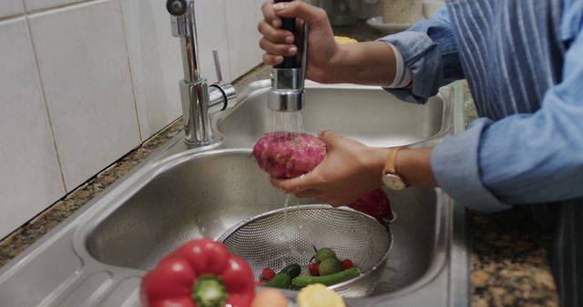 Person washing vegetables in kitchen sink, ensuring cleanliness. Promotes healthy eating and home cooking. Useful for content related to healthy lifestyle, cooking, kitchen hygiene, and meal preparation tips.