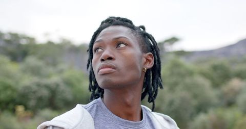 Contemplative young man with dreadlocks looking upward in soft outdoor bokeh landscape