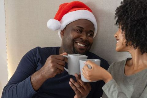 African american couple sharing cozy christmas morning coffee in bed wearing santa hat